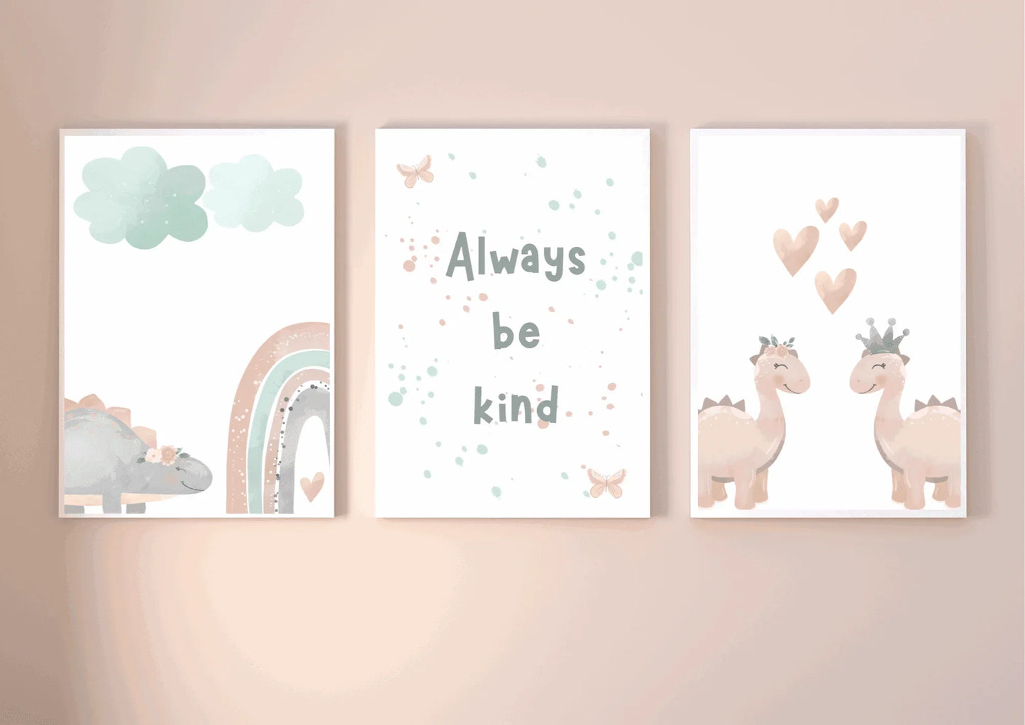 Three framed watercolor prints: a sleepy dinosaur with rainbow and clouds, an "Always Be Kind" typography print, and two crowned pink dinosaurs with hearts.