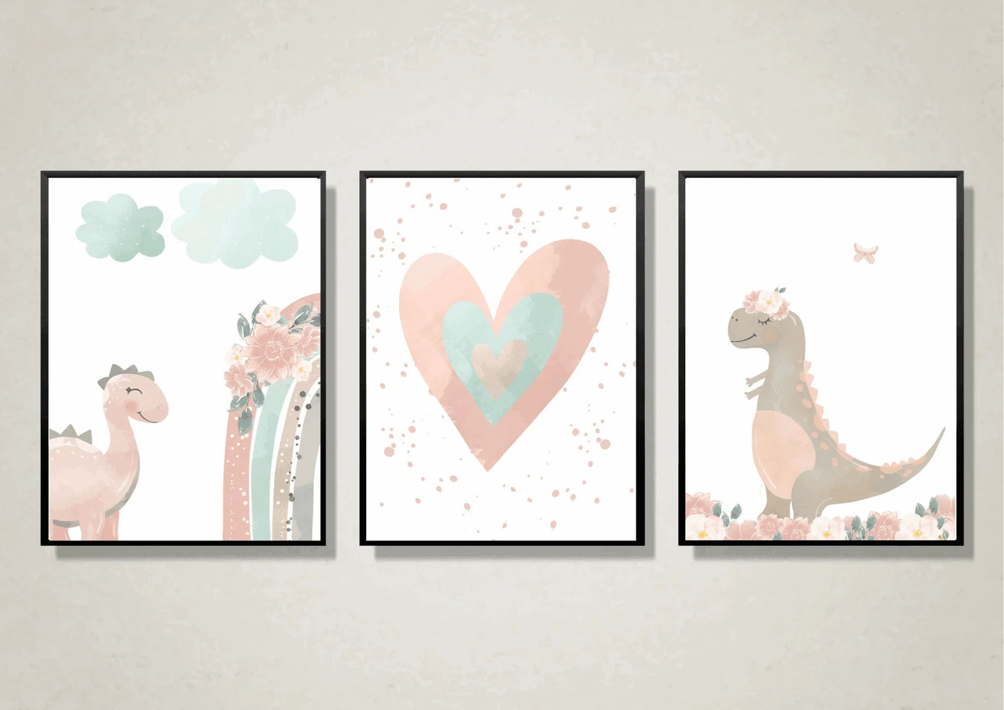 A close-up view of three framed art prints hanging on a light, textured wall. The prints are a whimsical, watercolor set featuring a pink dinosaur, a pink and teal heart, and a gray dinosaur with a floral crown. Each is framed in a thin black frame.