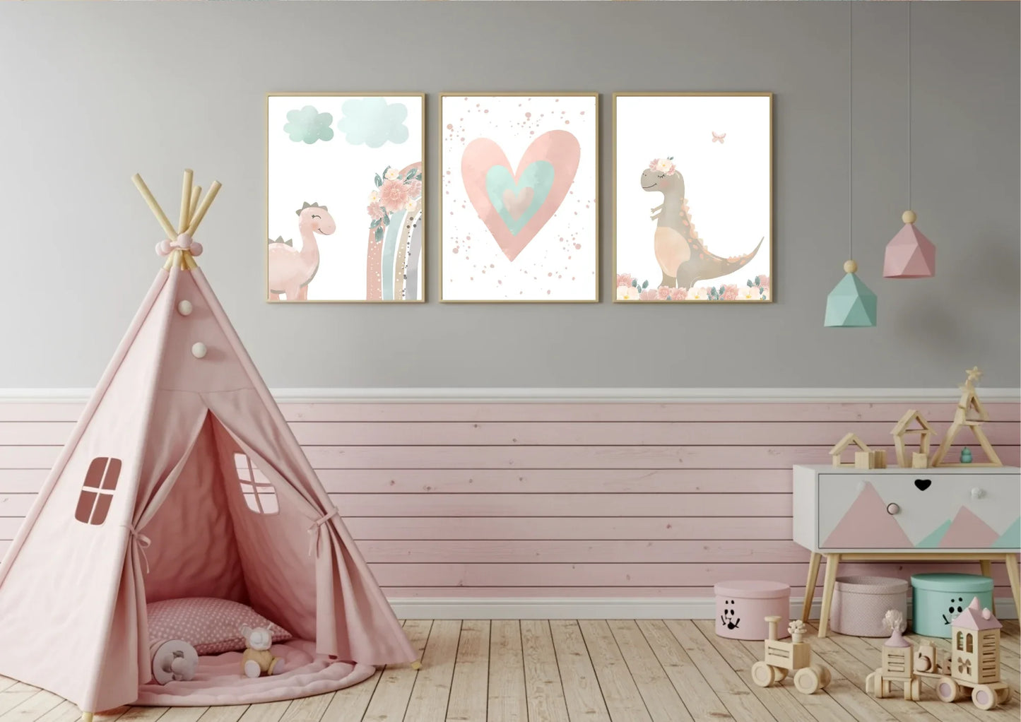 A set of three framed nursery prints featuring a pink dinosaur, a rainbow, a large heart, and a dinosaur with a floral crown, hanging on a gray and pink slatted wall. A pink teepee tent is on the left, and a white and pink dresser with various toys is on the right.
