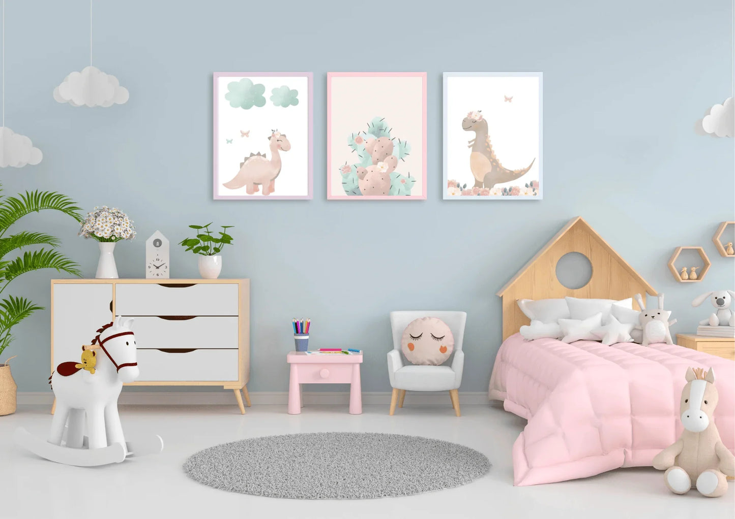 Three framed pastel dinosaur and cactus prints hanging on a light blue wall above a dresser and a child's bed with pink bedding.