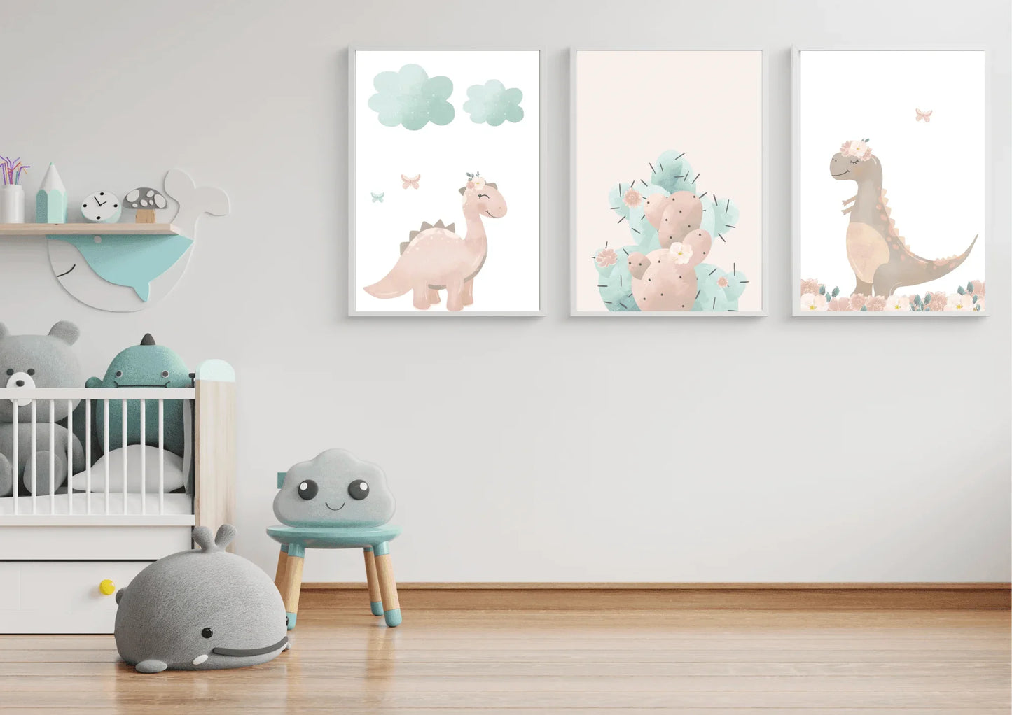 Three framed pastel dinosaur and cactus art prints on a white wall above a baby crib and a whale-themed wall shelf.
