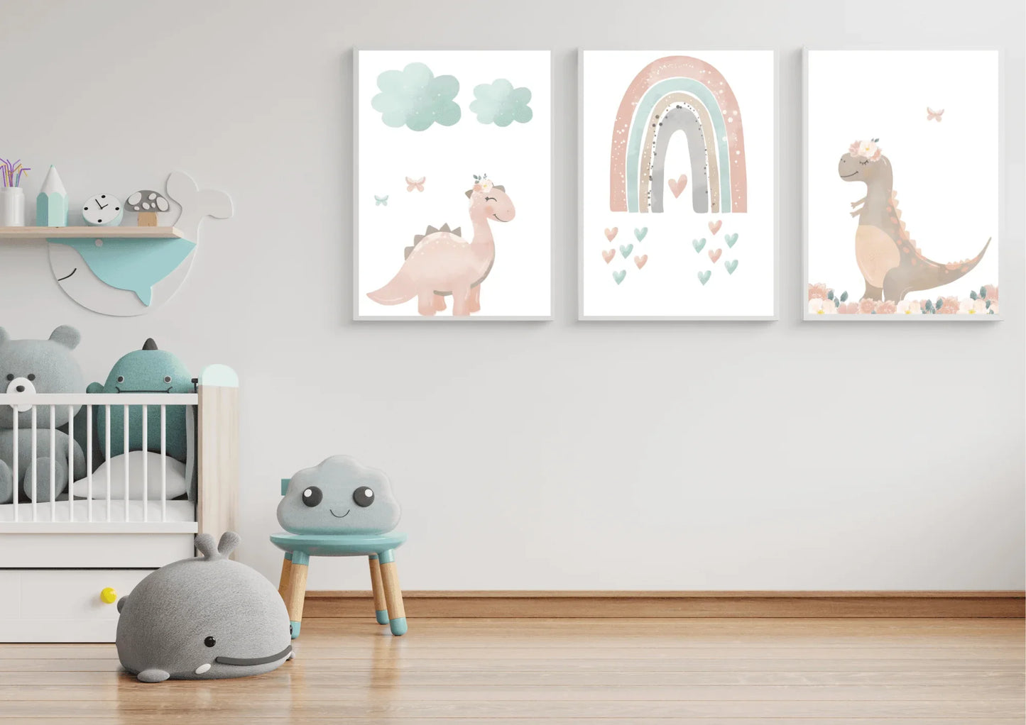 A minimalist child's room with white walls and a light wood floor. A set of three digital art prints featuring pastel dinosaurs and a rainbow hangs on the wall above a crib filled with stuffed animals. A small blue stool with a smiling cloud face and a gray whale-shaped plush toy are on the floor.