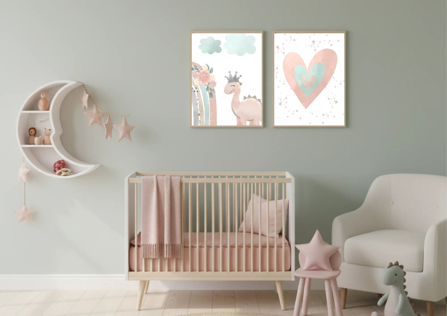 A charming baby girl's nursery featuring a white crib with pink bedding, a cozy armchair, and a crescent moon shelf. On the wall, two framed digital prints depict a cute pink dinosaur with a crown and a watercolor heart, all against a soft sage green wall.