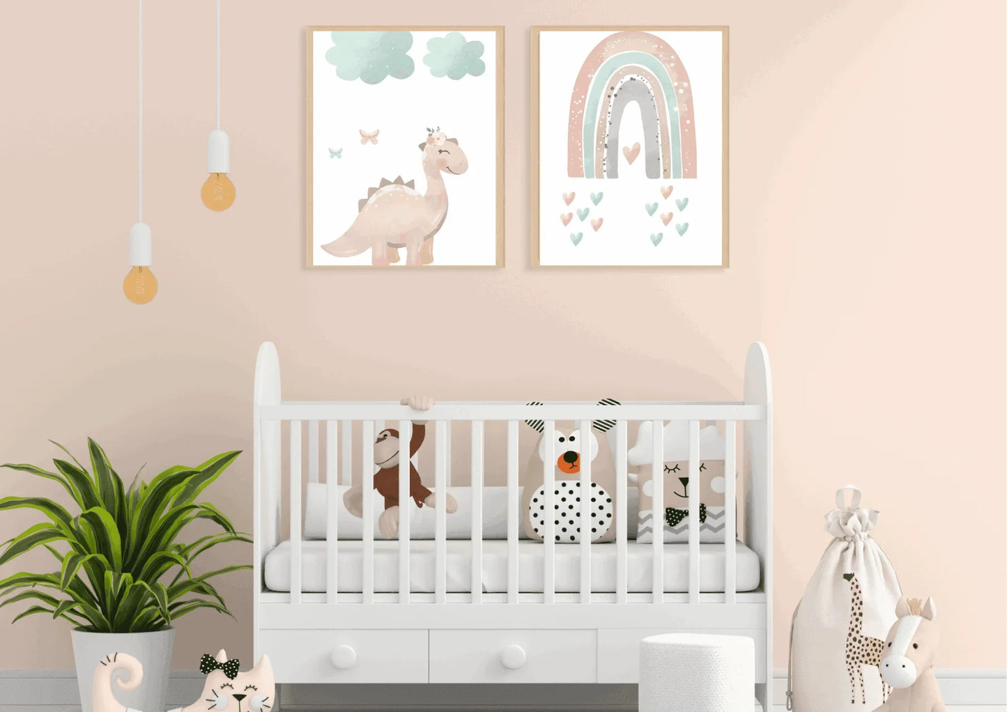 Two framed pastel prints (pink dinosaur with clouds, and a rainbow with hearts) on a light peach wall above a white baby crib.