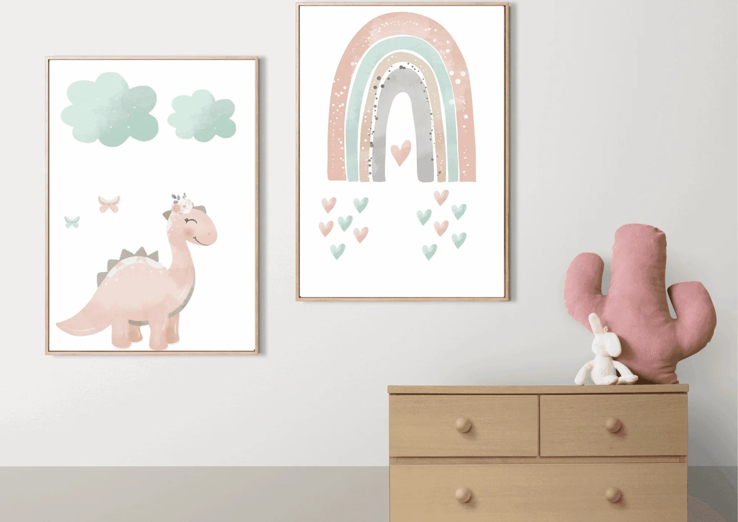 DinosTwo framed pastel prints (pink dinosaur with clouds, and a rainbow with hearts) on a white wall above a wooden dresser.aur nursery prints