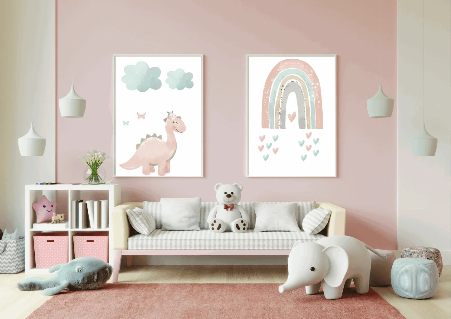 Two framed pastel prints (pink dinosaur with clouds, and a rainbow with hearts) on a pink wall above a couch with a teddy bear in a child's room.