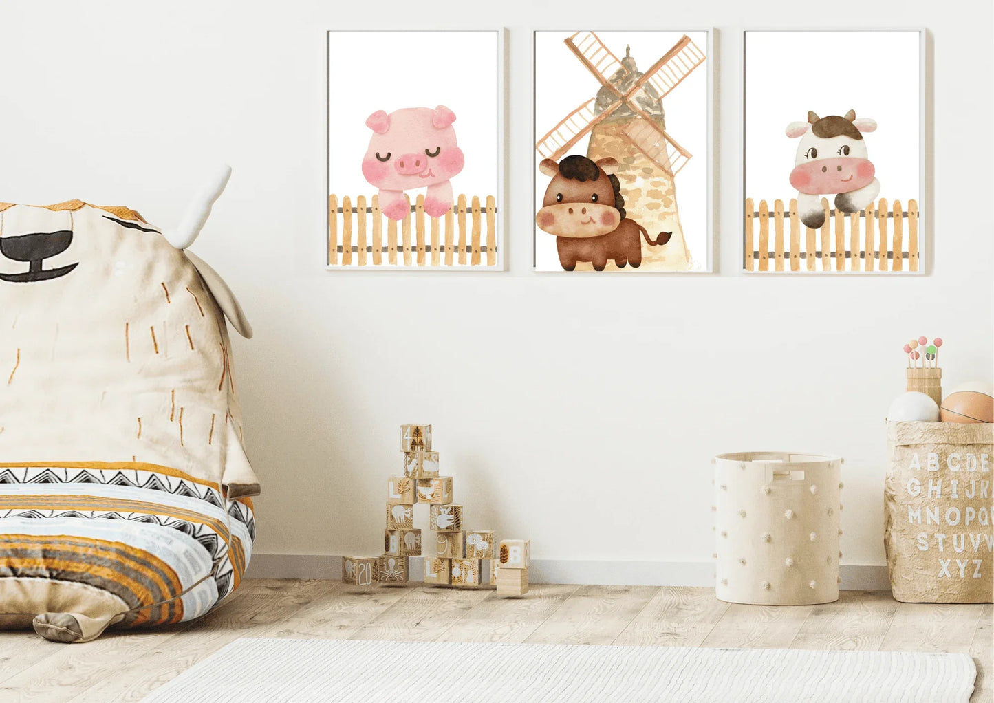 Three framed watercolor farm animal prints (pig, horse, cow) hanging on a white wall in a child's playroom with a large beanbag, wooden blocks, and a storage basket.