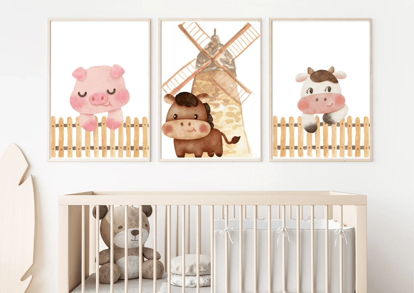 Three framed watercolor farm animal prints (pig, horse with windmill, cow) hanging above a wooden baby crib with a teddy bear inside.
