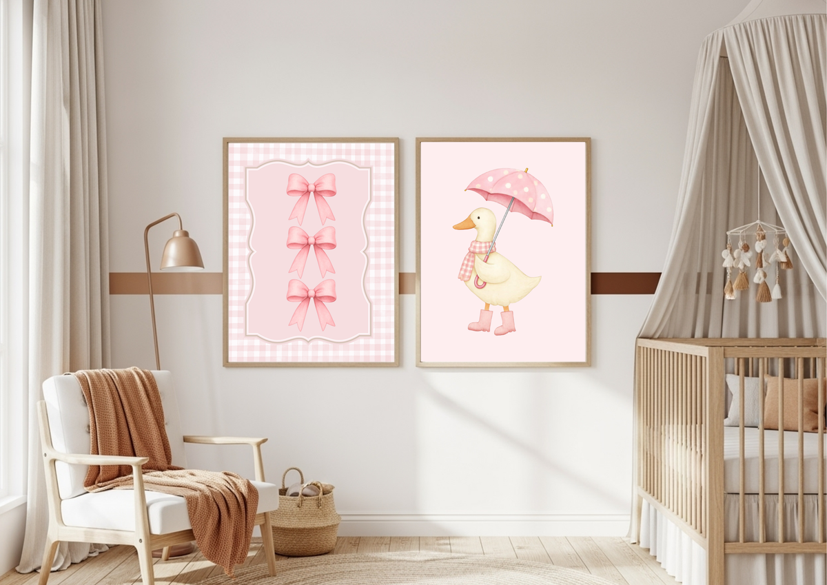 A styled nursery interior with two framed wall art prints hanging on a light wall above a wooden crib and chair. The left print shows pink bows on a pink gingham background, and the right print shows a yellow duck holding a pink umbrella.