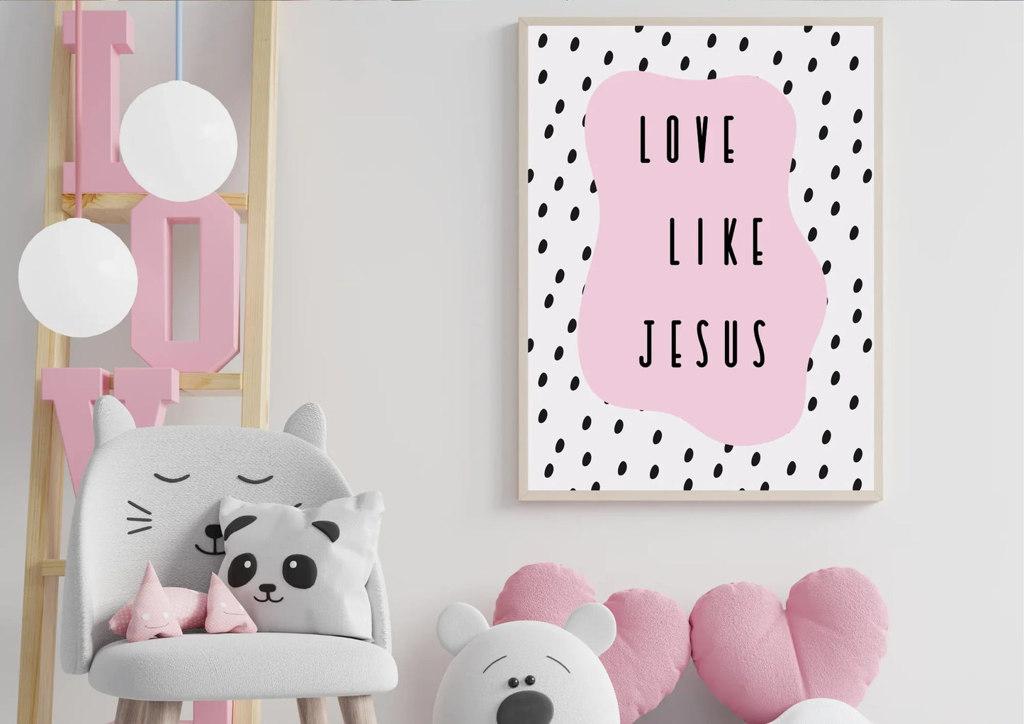 A wooden-framed art print with the quote "Love like Jesus" on a white wall in a child's room with a cat chair and a "LOVE" sign.