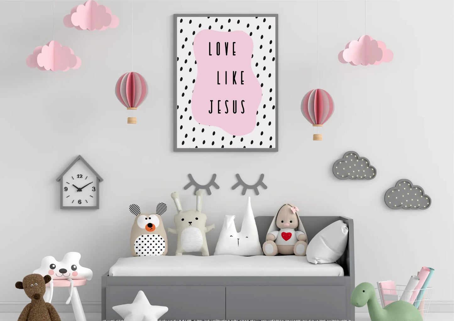 A framed "Love like Jesus" art print on a gray wall in a child's room, surrounded by whimsical clouds and hot air balloon decorations.
