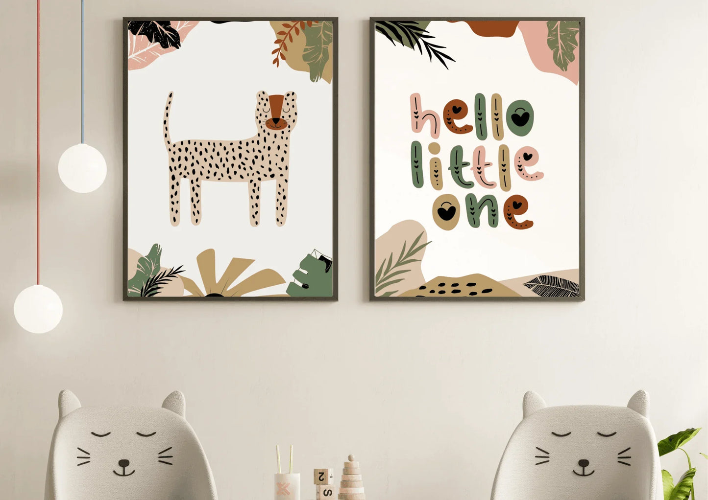 A simple, bright room with a two-piece framed art set of a boho jungle theme, with a cheetah/leopard print and "hello little one." The prints hang above two cat-ear-shaped children's chairs with light grey fabric.