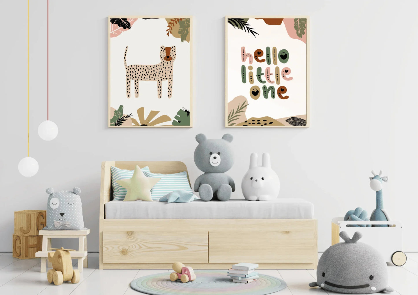 A child's room featuring a small wooden bed with storage drawers and several stuffed toys. A two-piece framed art set with a boho jungle theme, including a cheetah/leopard print and "hello little one," hangs above the bed.