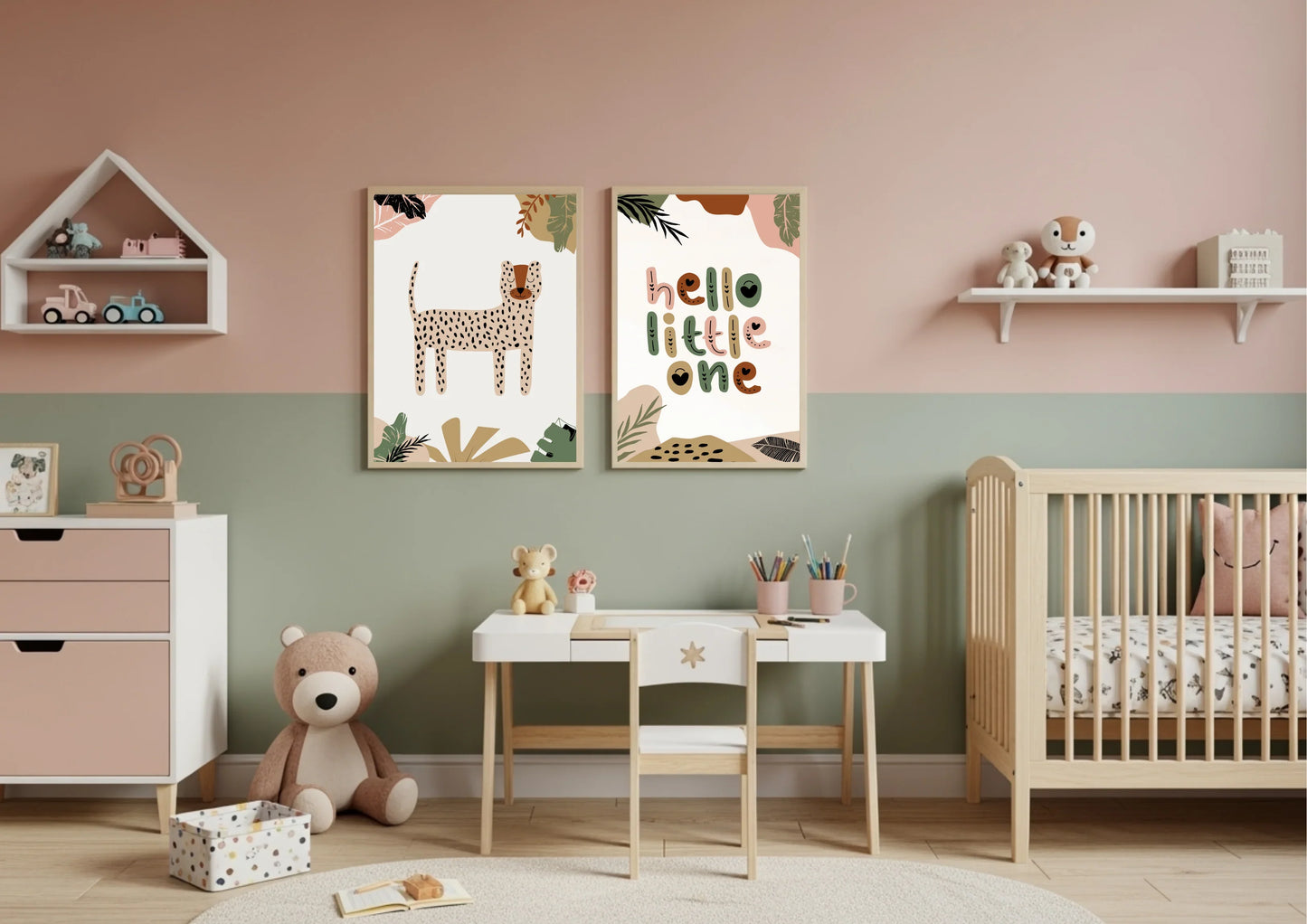 A nursery with a two-toned wall, featuring pink on top and sage green on the bottom. A two-piece framed art set with a boho jungle theme hangs in the center, above a small white wooden desk and chair. A wooden crib is on the right.