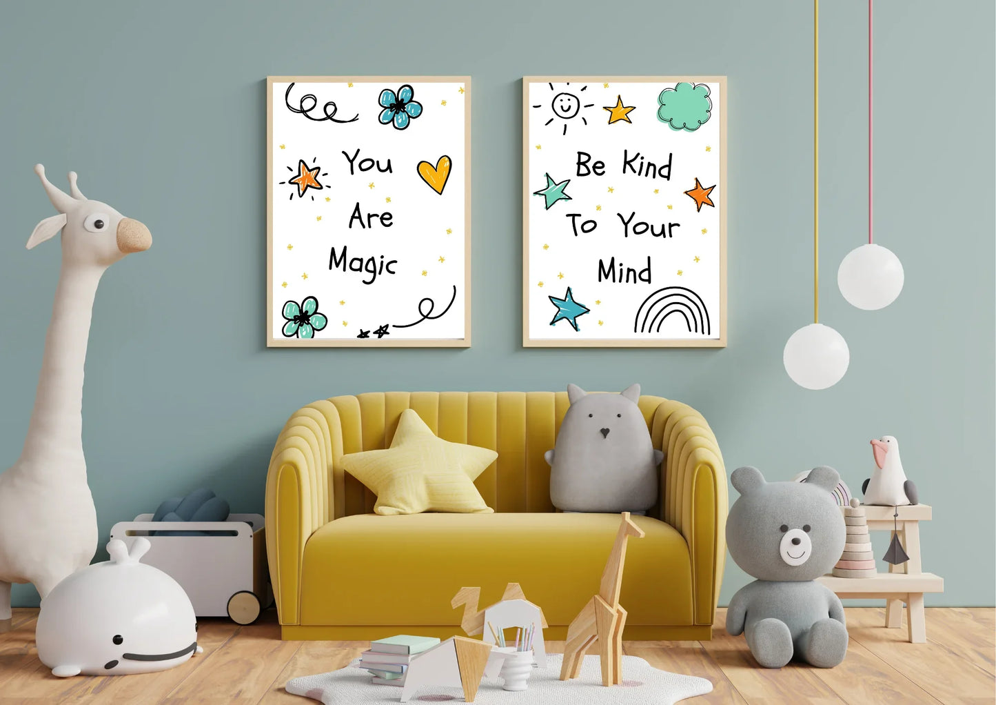 A pair of framed digital art prints with whimsical doodles and motivational quotes, hanging on a blue wall above a yellow couch in a child's room. The left print says "You Are Magic" and the right says "Be Kind To Your Mind." A large stuffed giraffe and various other toys are on the floor.