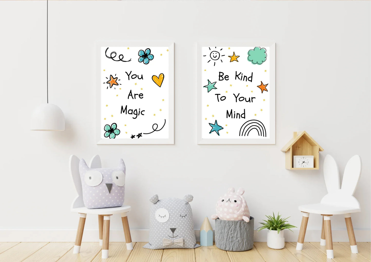 A pair of framed digital art prints with doodles and positive affirmations, hanging on a white wall. The left print says "You Are Magic" and the right says "Be Kind To Your Mind." Below the prints are two white wooden chairs, a small table, a pillow, and a small potted plant.