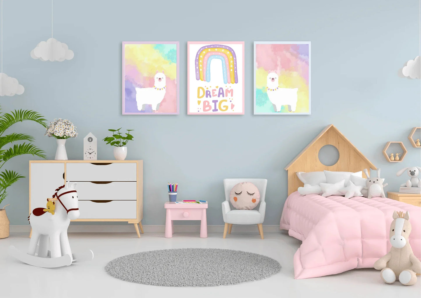 A set of three framed art prints with two llamas and a "Dream Big" quote on a light blue wall in a child's bedroom with a house-shaped bed.