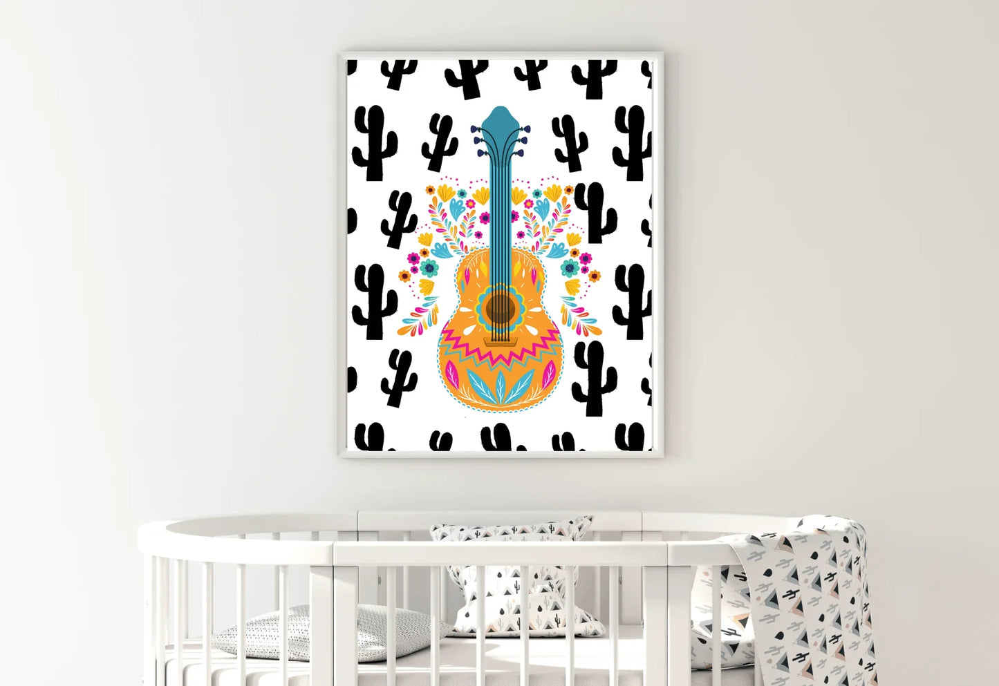A framed boho folk art guitar print with a black cactus background, hanging on a white wall above a white wooden crib.