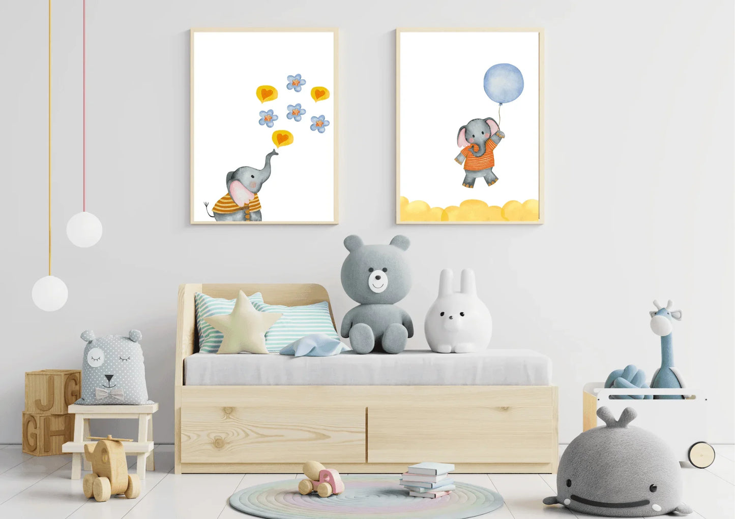 A close-up view of a child's bed with an under-drawer storage unit, surrounded by plush toys including a teddy bear and a rabbit. Two framed watercolor elephant prints are hung above the bed, one showing an elephant blowing hearts and flowers, and the other showing an elephant flying with a blue balloon.