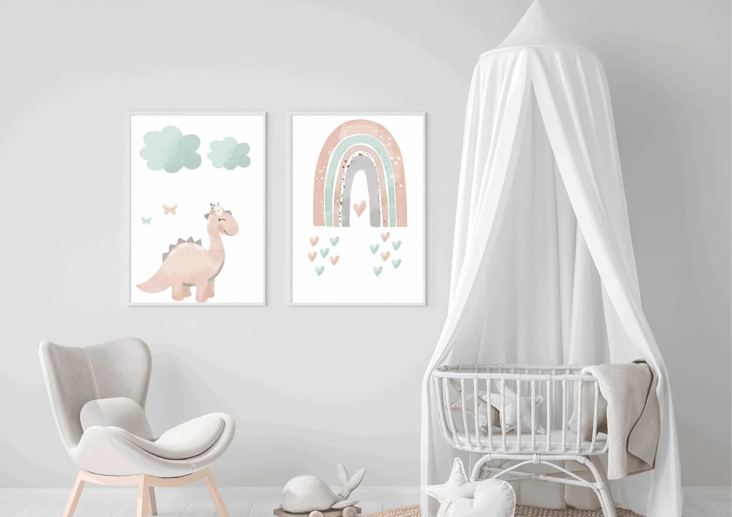 Two framed pastel prints (pink dinosaur with clouds, and a rainbow with hearts) on a white wall next to a baby crib with a canopy.