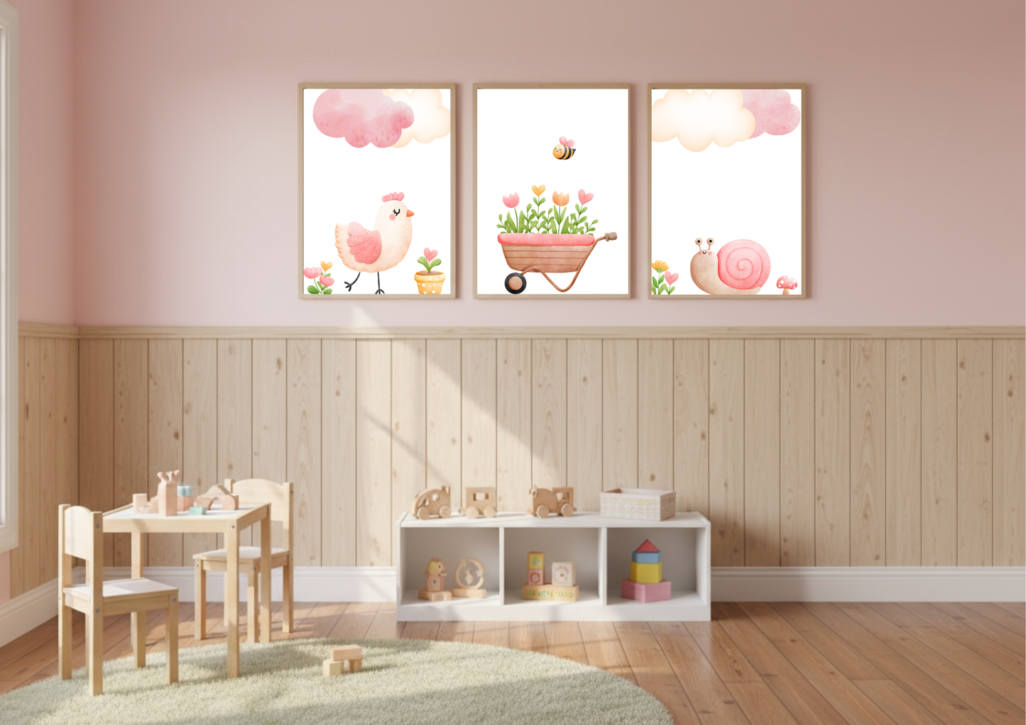 A child's play area with pink upper walls and natural wood wainscoting below. The room features a small wooden table and chairs, and a low white cubby shelf holding toys. A set of three Farm Nursery prints is displayed above the wainscoting, featuring a pink chick, a wheelbarrow of flowers with a bee, and a pink snail.