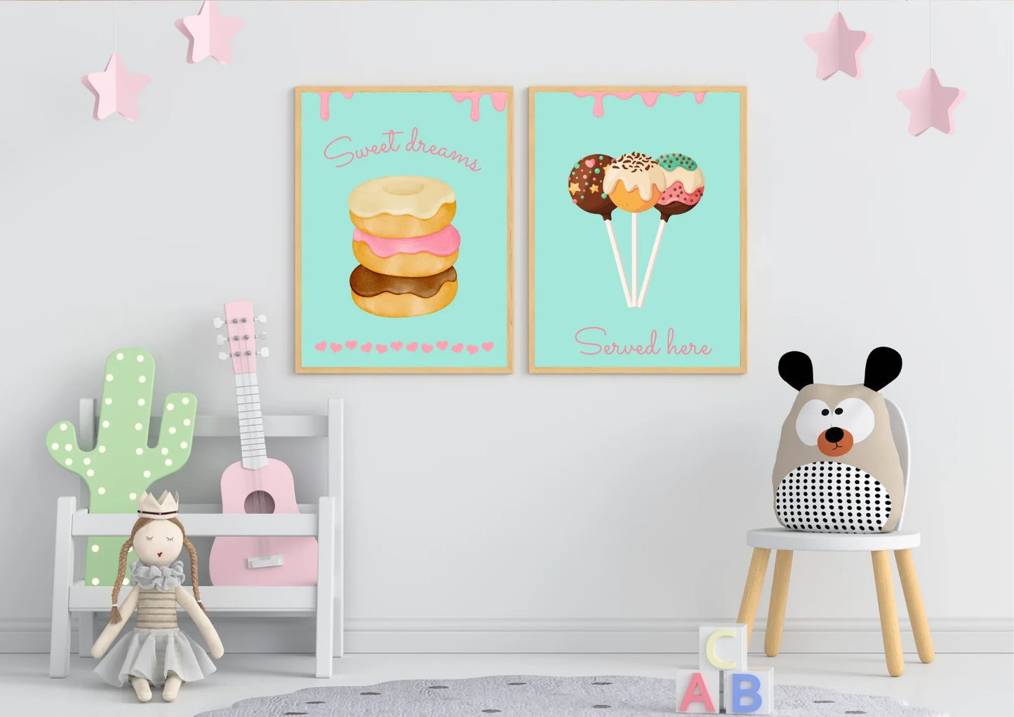 A set of two framed art prints of donuts and cake pops on a white wall in a child's playroom with toys.