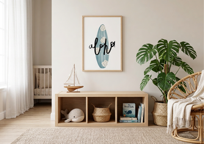 A bright, sunlit coastal-themed nursery featuring a light natural wood storage bench centered against a cream wall. Above the bench hangs a vertical wooden-framed print of a turquoise surfboard with white monstera leaves and the word "aloha" in black script. To the right, a large Monstera Deliciosa plant sits in a seagrass basket next to a rattan chair draped with a cream throw. The bench's cubbies hold a plush whale, a woven basket, and children's books, with a small wooden model sailboat resting on top.
