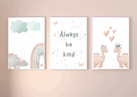Three framed watercolor prints: a sleepy dinosaur with rainbow and clouds, an "Always Be Kind" typography print, and two crowned pink dinosaurs with hearts.
