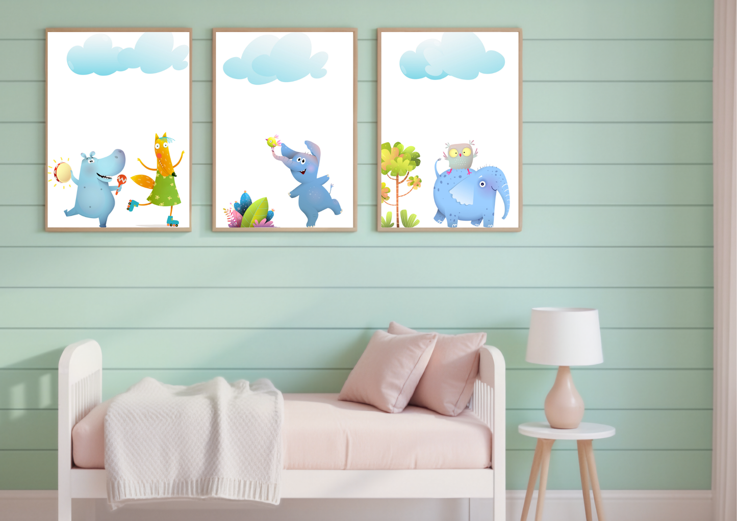 
A set of three whimsical animal art prints with wooden frames on a green plank wall above a daybed in a child's bedroom.