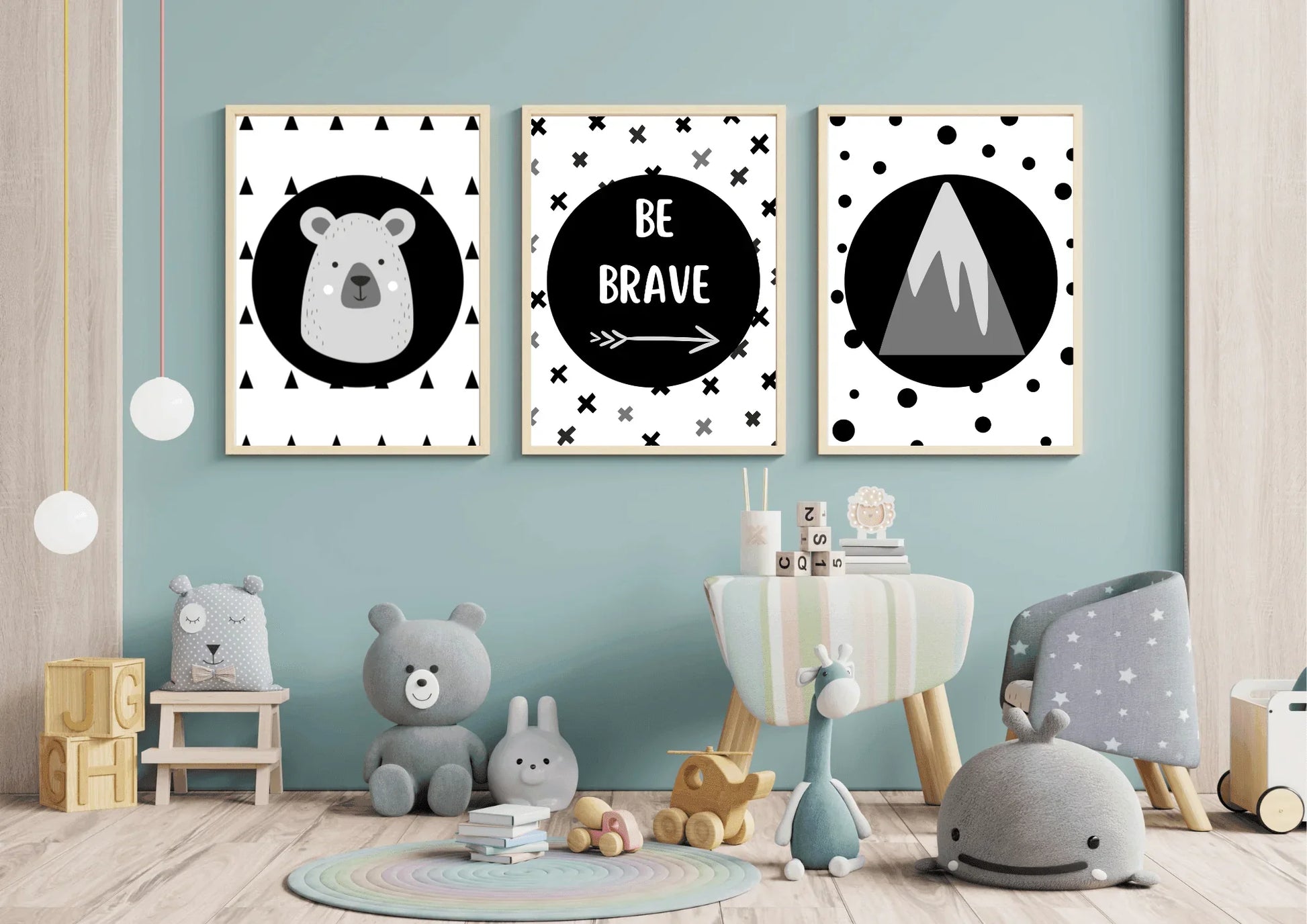 
Three framed monochrome nursery prints, depicting a bear, "Be Brave" text, and a mountain, hanging on a light blue wall above a variety of stuffed animals and a small chair.