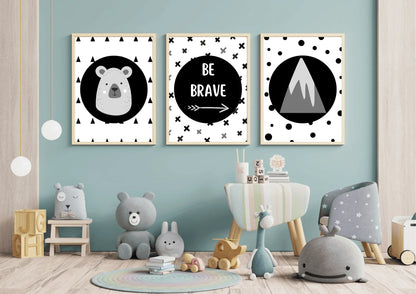 
Three framed monochrome nursery prints, depicting a bear, "Be Brave" text, and a mountain, hanging on a light blue wall above a variety of stuffed animals and a small chair.