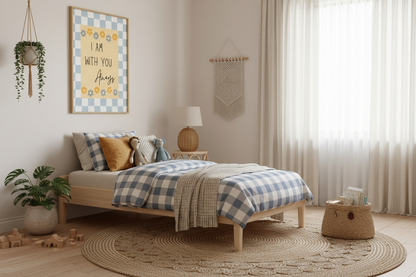 A child's bedroom with a light wood bed dressed in blue and white checkered bedding. The framed "I Am With You Always" Christian nursery art hangs above the bed. The room features a large round jute rug, hanging and potted plants, a woven bedside lamp, and a macrame wall hanging.