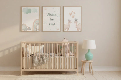 Three framed pastel dinosaur and "Always Be Kind" prints on a beige wall above a wooden baby crib with a mint green lamp on a stool.