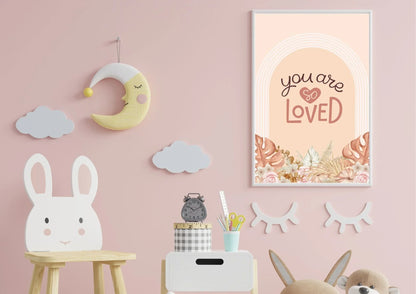 
A framed "You are so LOVED" boho art print on a pink wall in a child's nursery with a sleepy moon and a bunny chair.