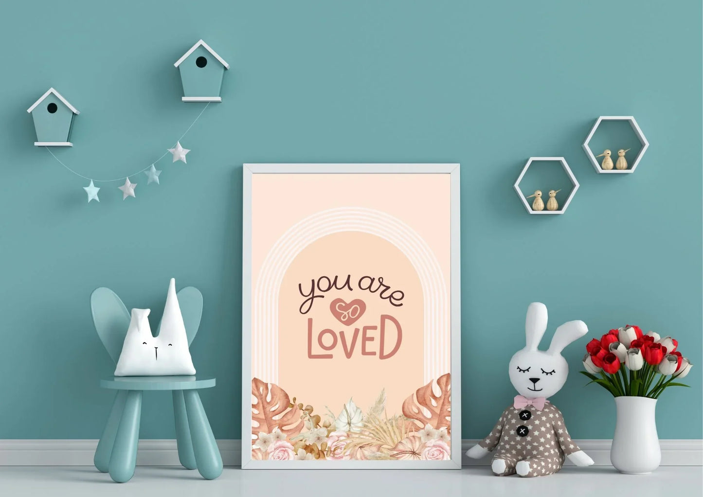 A framed "You are so LOVED" boho art print on a light blue wall in a child's playroom with a stuffed bunny and birdhouses.
