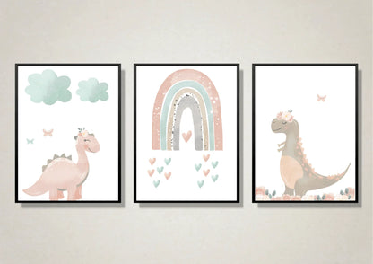 A trio of digital art prints for a nursery, each framed in a black frame. The first print on the left features a smiling, pastel pink dinosaur with a floral crown, standing under two light blue clouds with two butterflies nearby. The middle print shows a pastel rainbow with a heart at its base and smaller hearts floating below. The third print on the right features a brown dinosaur with a floral crown, standing in a field of flowers, with a butterfly flying above.