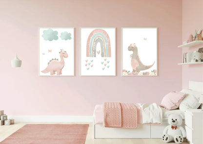 A child's bedroom with light pink walls and a matching pink rug. A set of three framed digital art prints hang above a small white bed with a pink blanket. The art features pastel pink and brown dinosaurs and a rainbow. A white teddy bear sits on the floor next to the bed.