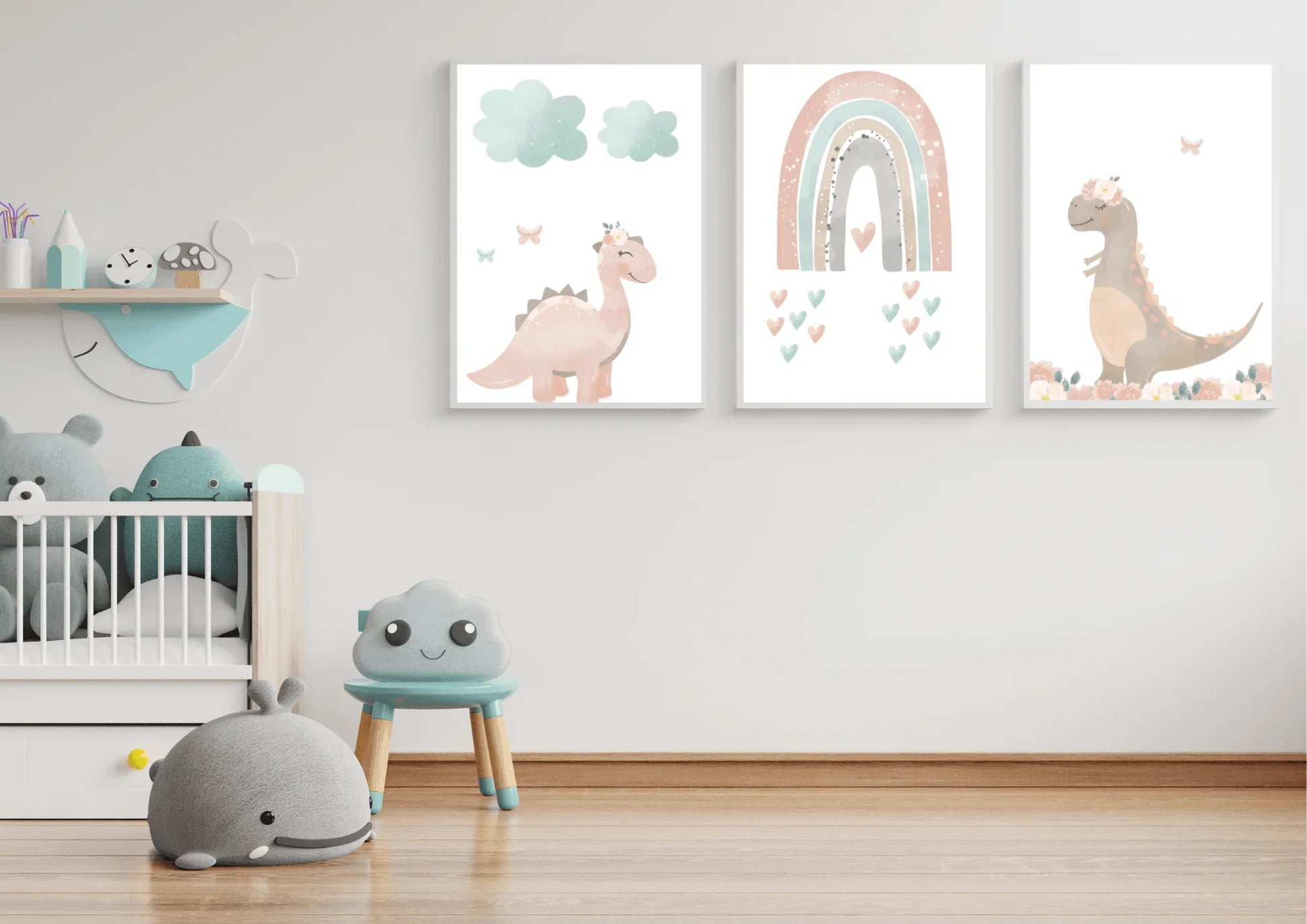 A minimalist child's room with white walls and a light wood floor. A set of three digital art prints featuring pastel dinosaurs and a rainbow hangs on the wall above a crib filled with stuffed animals. A small blue stool with a smiling cloud face and a gray whale-shaped plush toy are on the floor.