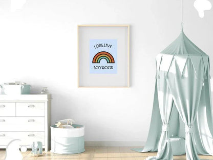 
A framed "Long Live Boyhood" retro rainbow print hanging on a white wall in a neutral-toned nursery, above a changing table and next to a bed with a canopy.