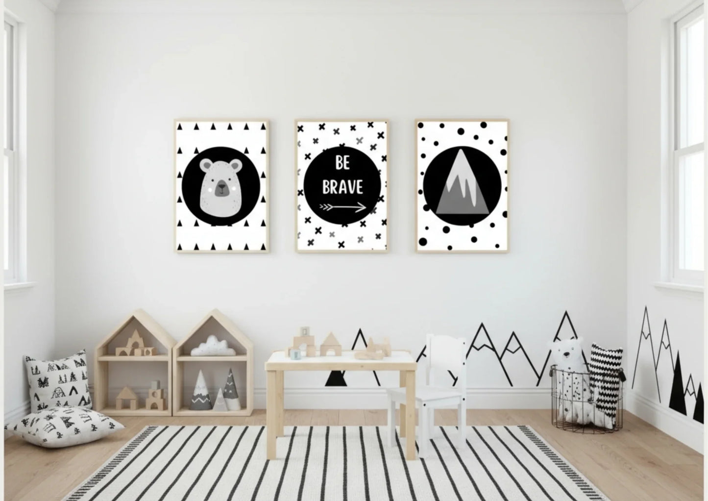 
Three framed monochrome nursery prints, depicting a bear, "Be Brave" text, and a mountain, hanging on a white wall above a small table and a rug with a black-and-white striped pattern.