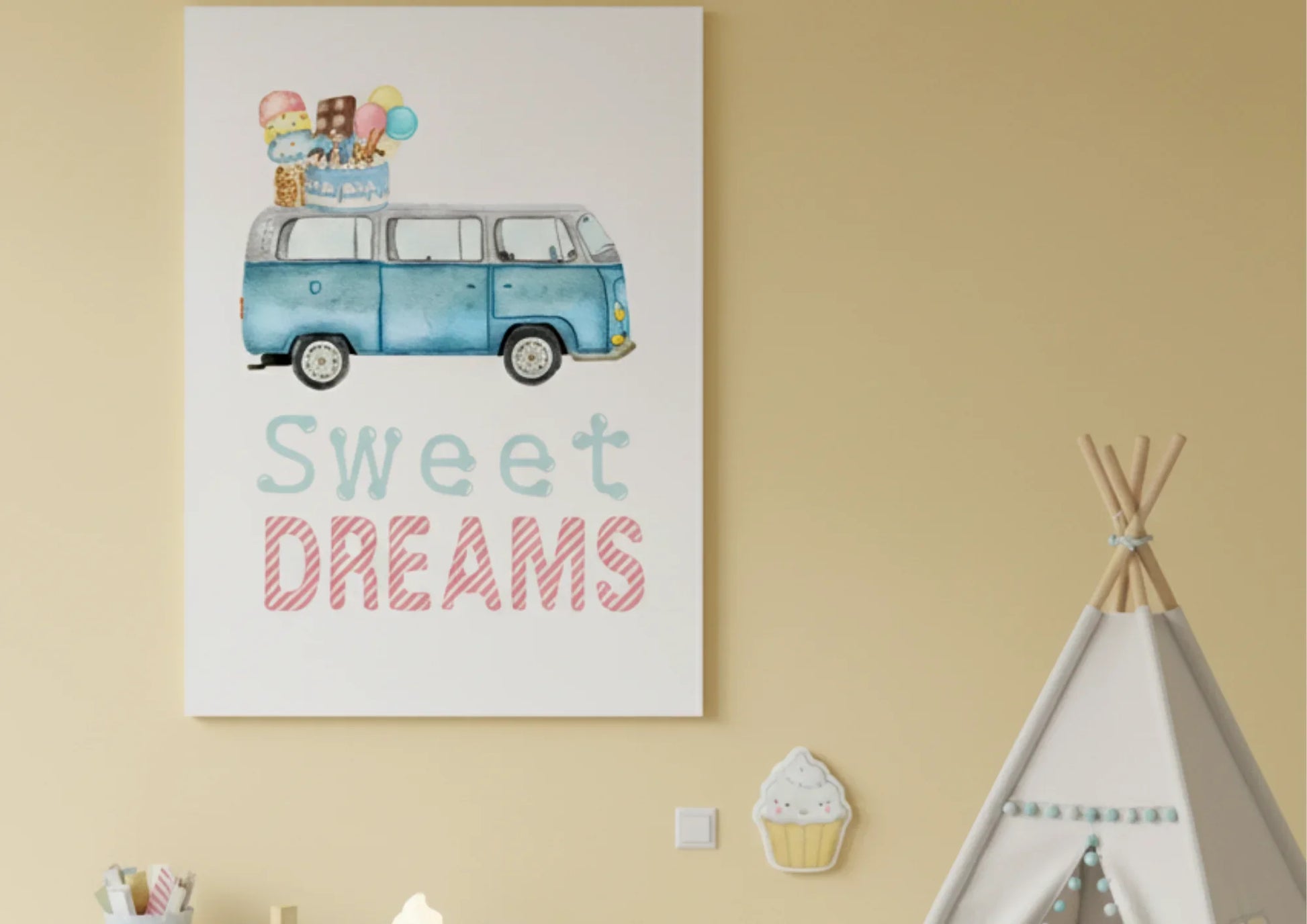 A close-up of a large canvas print hanging on a pale yellow wall. The artwork is a watercolor illustration of a blue, vintage Volkswagen van (VW bus) with a stack of ice cream cones, popsicles, and a birthday cake on its roof. Below the image, the text "Sweet DREAMS" is written in a playful font, with "Sweet" in light blue and "DREAMS" in striped pink. To the right, the top of a canvas teepee with light wood poles is visible. Below the artwork, a small cupcake-shaped wall decal is stuck to the wall.