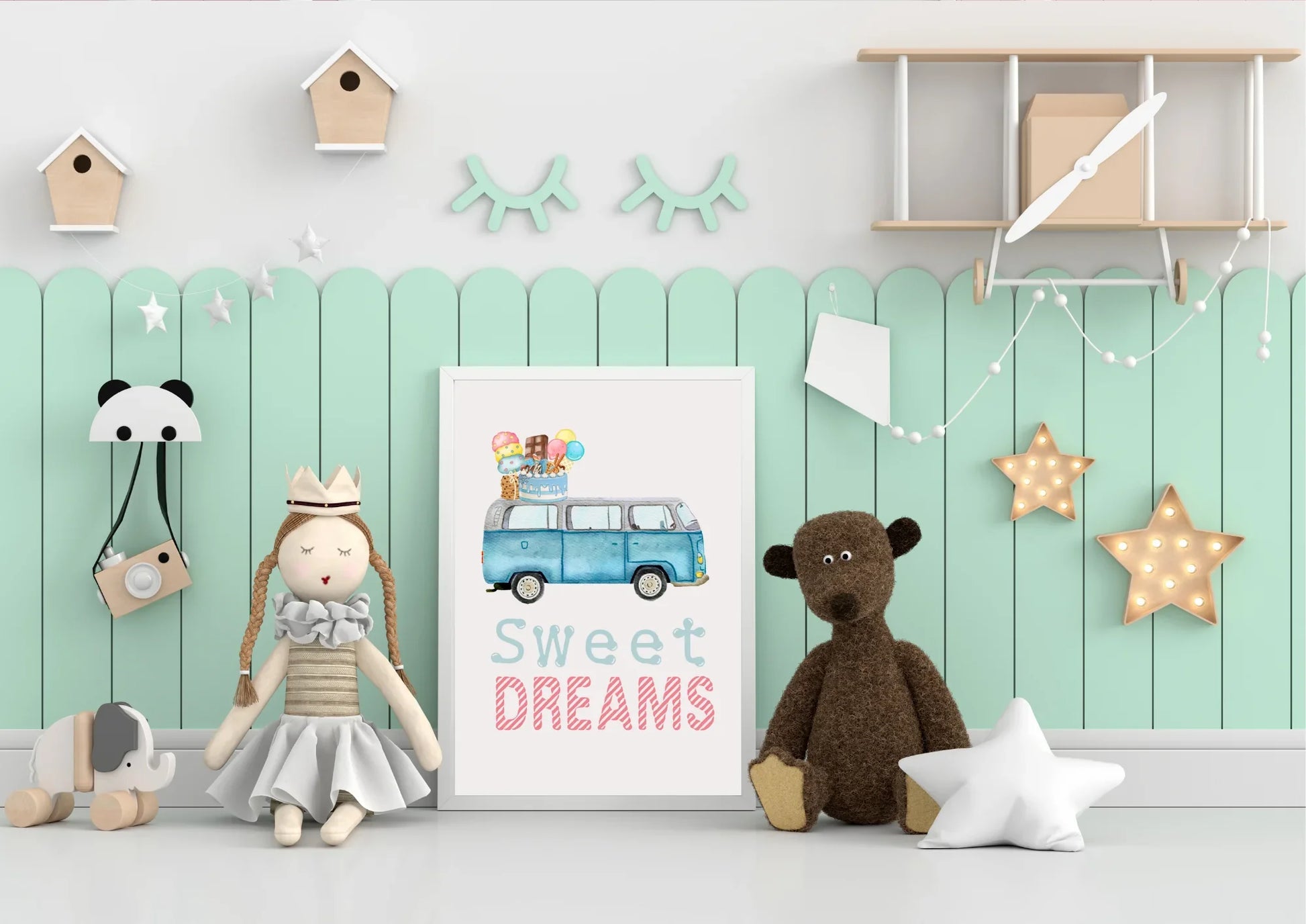 A child's room setup featuring a white wall with a mint green wainscoting or paneling running across the center. A framed art print rests on the floor against the paneling, showing a blue, vintage Volkswagen van (VW bus) with a stack of ice cream cones, popsicles, and a birthday cake on its roof, and the text "Sweet DREAMS" in light blue and pink below it.