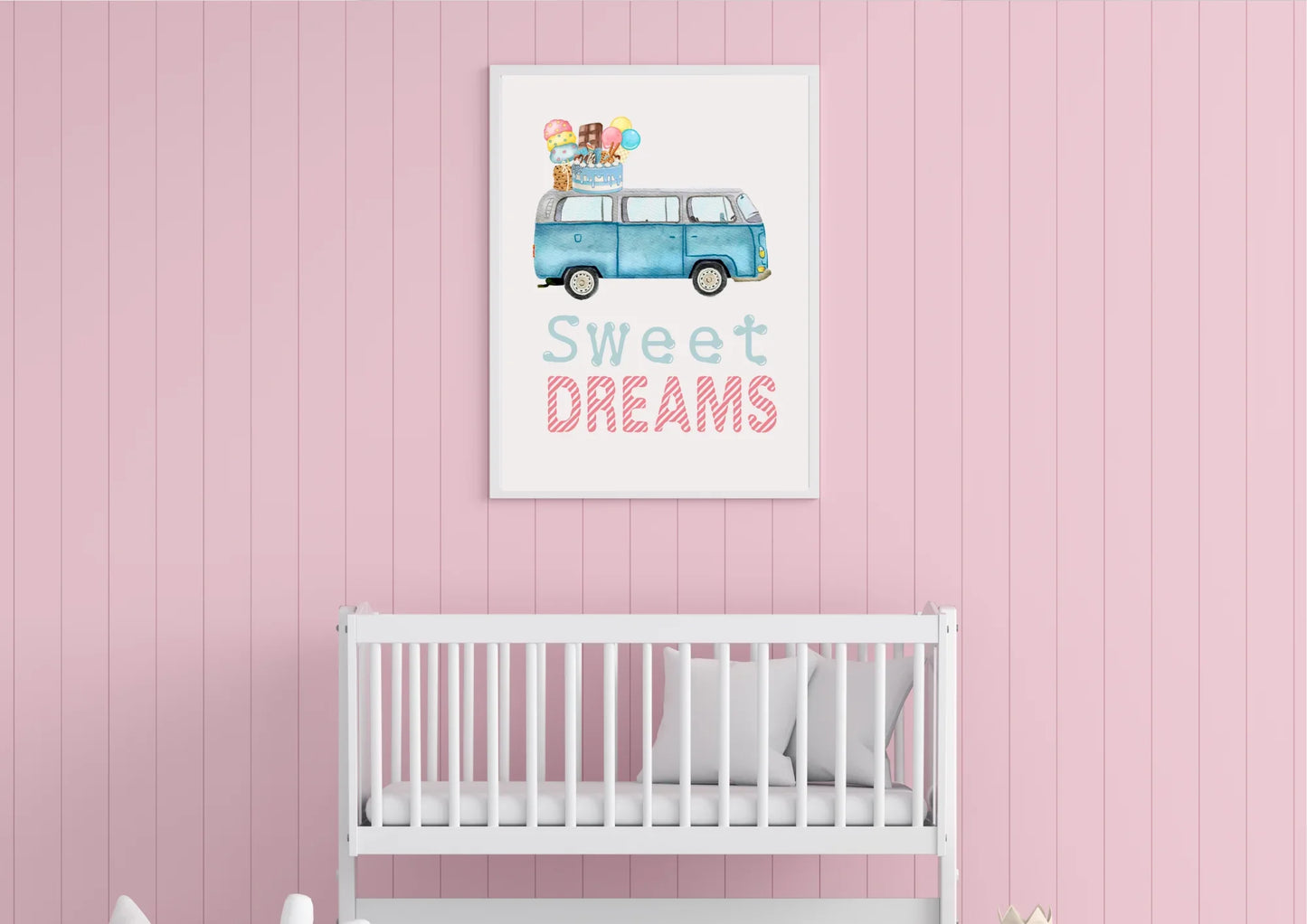 A brightly lit image of a framed art print hanging directly over a white wooden baby crib. The wall behind is covered in vertical pink wood paneling or shiplap. The artwork is a watercolor illustration of a blue, vintage Volkswagen van (VW bus) with a stack of ice cream cones, popsicles, and a birthday cake on its roof. Below the image, the text reads "Sweet DREAMS" in a playful font, with "Sweet" in light blue and "DREAMS" in striped pink. The crib contains white bedding and a pillow.