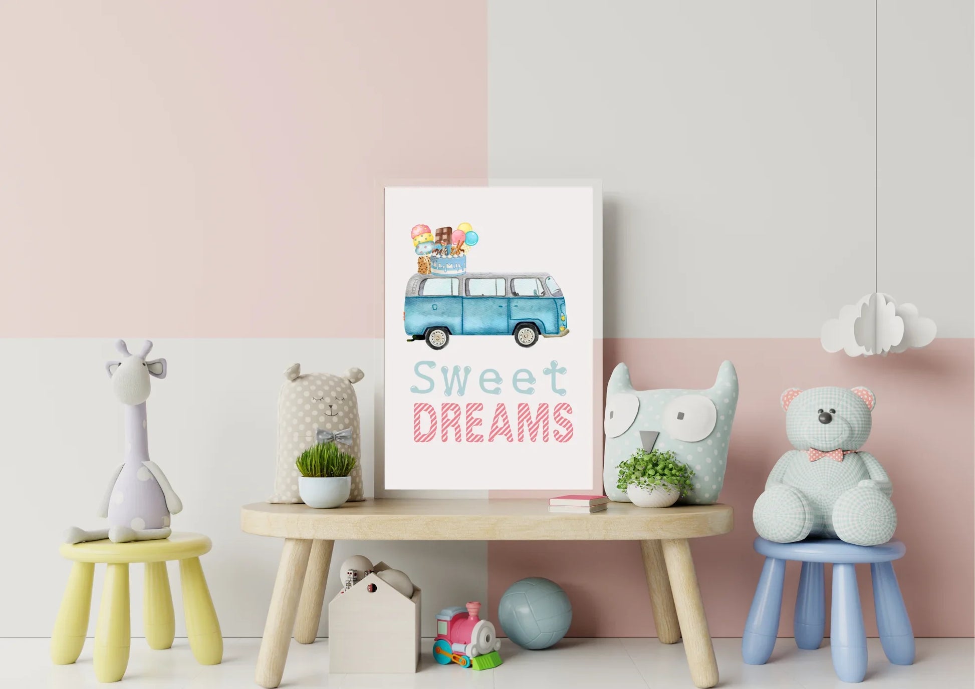 A framed art print is displayed on a small, light wood play table in a child's room. The wall behind is painted with a horizontal color block design—the top half is pale pink and the bottom half is off-white. The artwork is a watercolor illustration of a blue, vintage Volkswagen van (VW bus) with a stack of ice cream cones, popsicles, and a birthday cake on its roof, and the text "Sweet DREAMS" in light blue and pink below it.