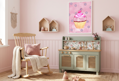 A photorealistic photograph of a cozy boho-themed nursery during a bright morning. The room features a soft, light pink wall with wainscoting and a light oak wood floor partially covered by a large round jute rug. In the center, a sage green play kitchen with wicker-inlay doors, light wood countertops, and a floral backsplash sits against the wall. To the left is a natural wood rocking chair with a cream-colored knit throw blanket and a dusty pink velvet pillow. Hanging prominently above the kitchen is a wh