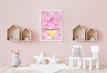 A photorealistic photograph of a bright and whimsical nursery with soft pink walls and a light wood floor. In the center of the wall hangs a white-framed vertical art print featuring a pink watercolor cupcake topped with a cherry and surrounded by small purple donuts on a pink cloudy background. Flanking the print are two pairs of natural wood house-shaped shelves containing small decorative items. Below, a white faux fur rug sits on the floor, accented by two large white star-shaped cushions. 