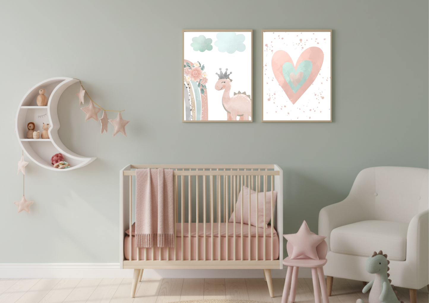 A charming baby girl's nursery featuring a white crib with pink bedding, a cozy armchair, and a crescent moon shelf. On the wall, two framed digital prints depict a cute pink dinosaur with a crown and a watercolor heart, all against a soft sage green wall.