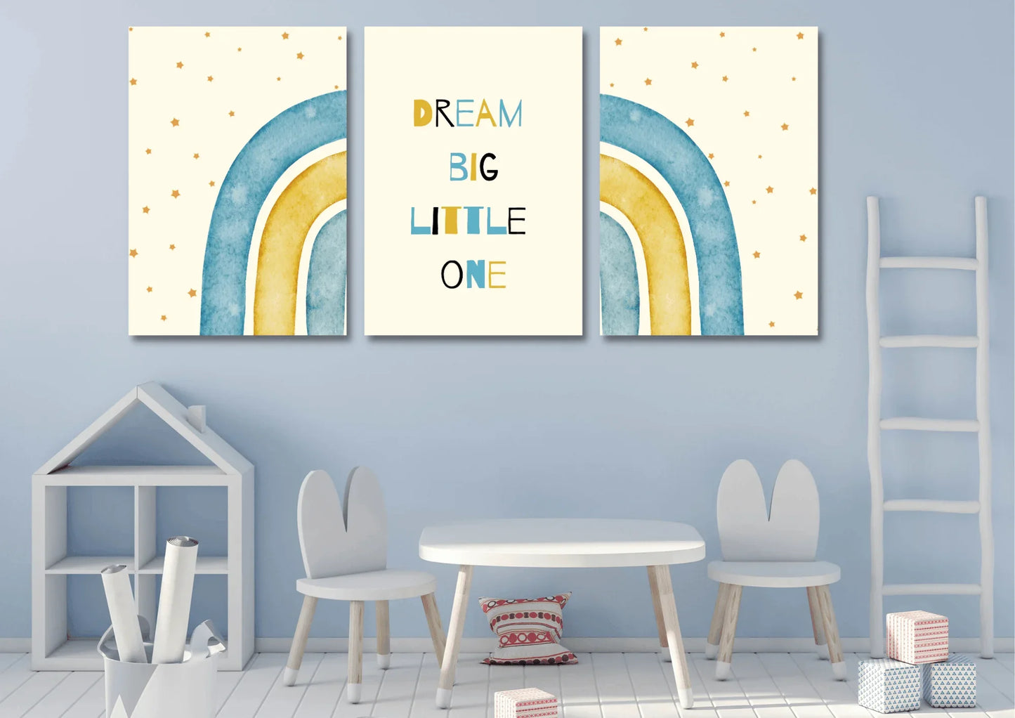 A three-piece nursery print set, featuring a "Dream Big Little One" message and blue and yellow watercolor rainbows, hanging on a light blue wall above a small table and children's chairs.