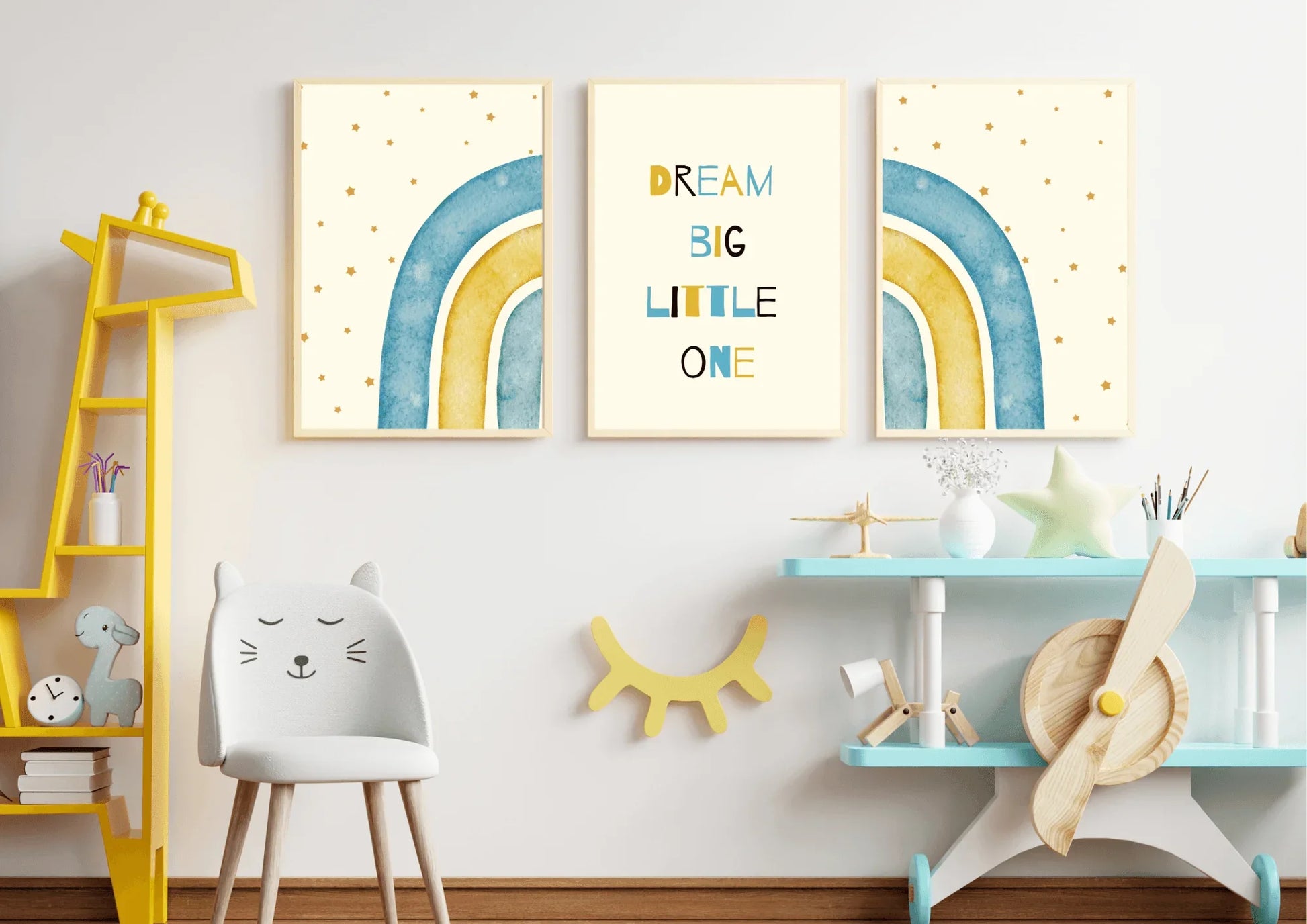 A three-piece framed nursery print set, featuring a "Dream Big Little One" message and blue and yellow watercolor rainbows, hanging on a white wall above a yellow bookshelf and a small chair.