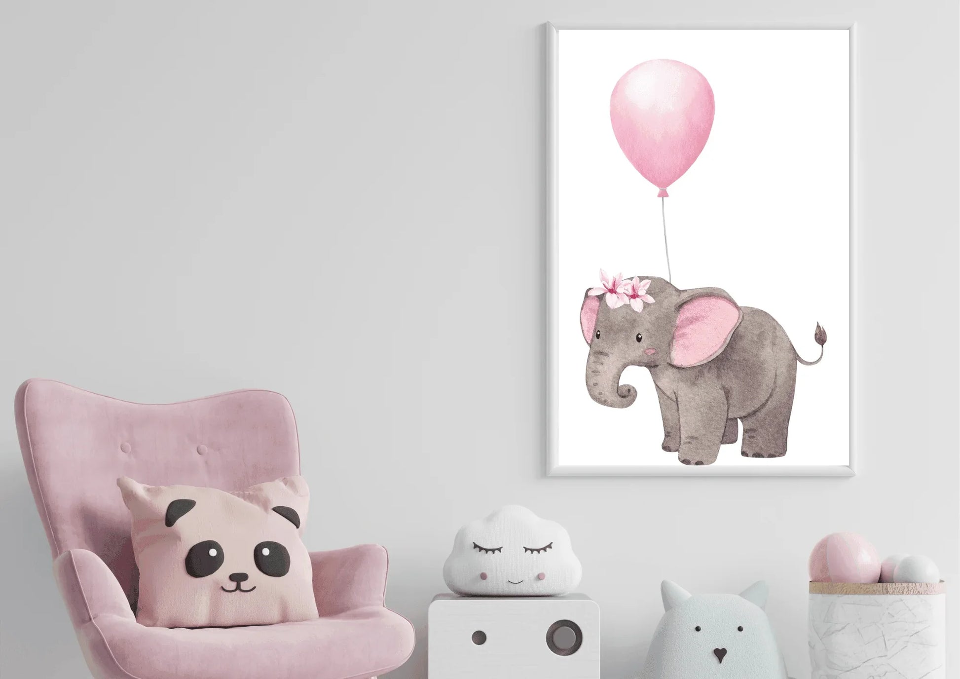 A framed nursery print of a baby elephant with a floral crown holding a pink balloon, hanging on a white wall above a pink armchair with a panda pillow.